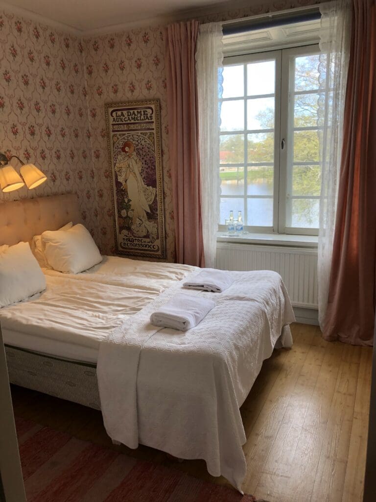Hotellrum med baddad sang, monstrad tapet och fonster mot parken